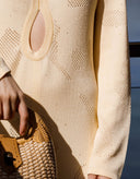 Close-up of a beige knitted dress with a textured pattern, held by a hand.