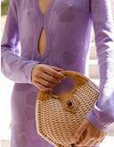 Person wearing a light purple dress holding a woven handbag.