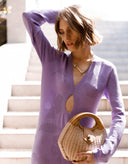 Woman in a purple dress holding a woven handbag on a staircase