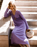 Woman in a purple dress sitting on steps with a woven handbag.