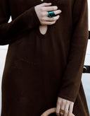 Person wearing a brown dress with a green ring on a white background