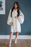 Woman wearing a white dress with bell sleeves against a blue wall.