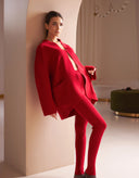 Woman in a red outfit standing against a beige wall.