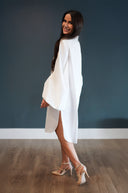 Woman wearing a white dress with a high slit on a plain background